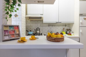A kitchen with white cabinets, a gas stove, a kettle, and a fruit bowl on the counter.