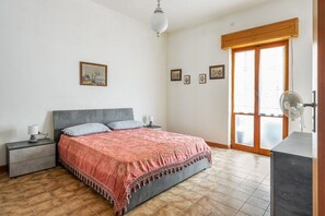 Ein Schlafzimmer mit Bett, Nachttischen, einem Schminktisch, einem Ventilator und einer Schiebetür.