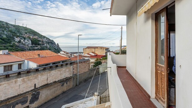 A residential balcony with a view of the sea and a hillside.