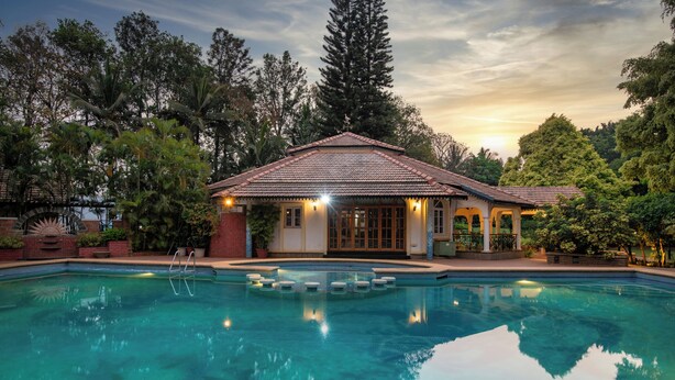 Une piscine dotée d’une terrasse carrelée, entourée d’une végétation luxuriante et bordée d’un bâtiment dont le toit est également recouvert de tuiles.
