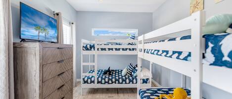 A child's bedroom with bunk beds, a ceiling fan, a TV, and a window with a view of palm trees.