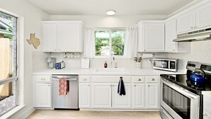 A kitchen with white cabinets, a microwave, a stove, and a window with curtains. - Minutes from downtown Austin! Cozy bungalow w/ fire pit; perfect for families! (Austin)