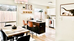 A modern kitchen with white cabinets, a wooden dining table, and a pink pendant light. - Minutes from downtown Austin! Cozy bungalow w/ fire pit; perfect for families! (Austin)