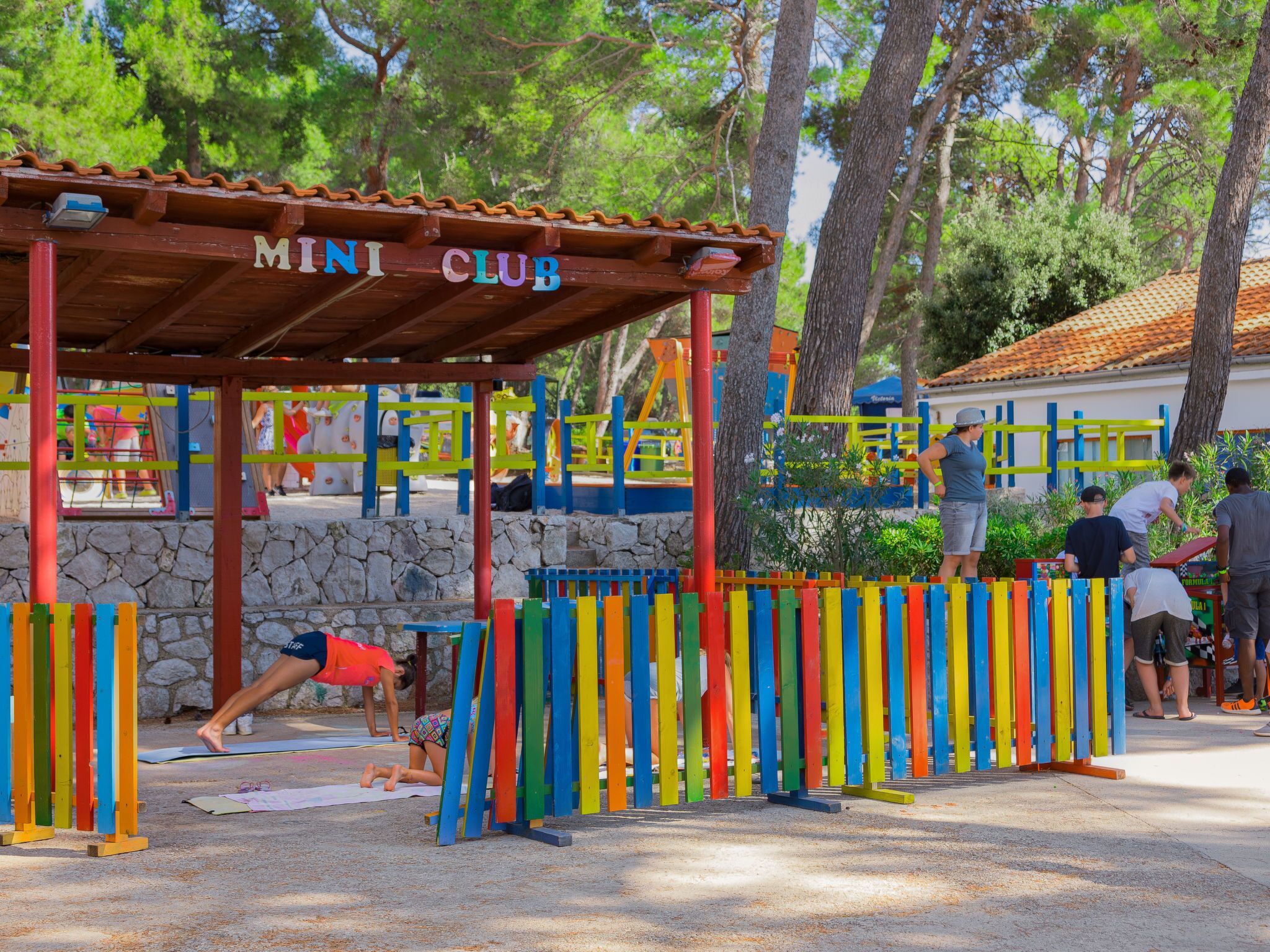A children's play area with a colorful fence and a covered seating area labeled 'MINI CLUB'.