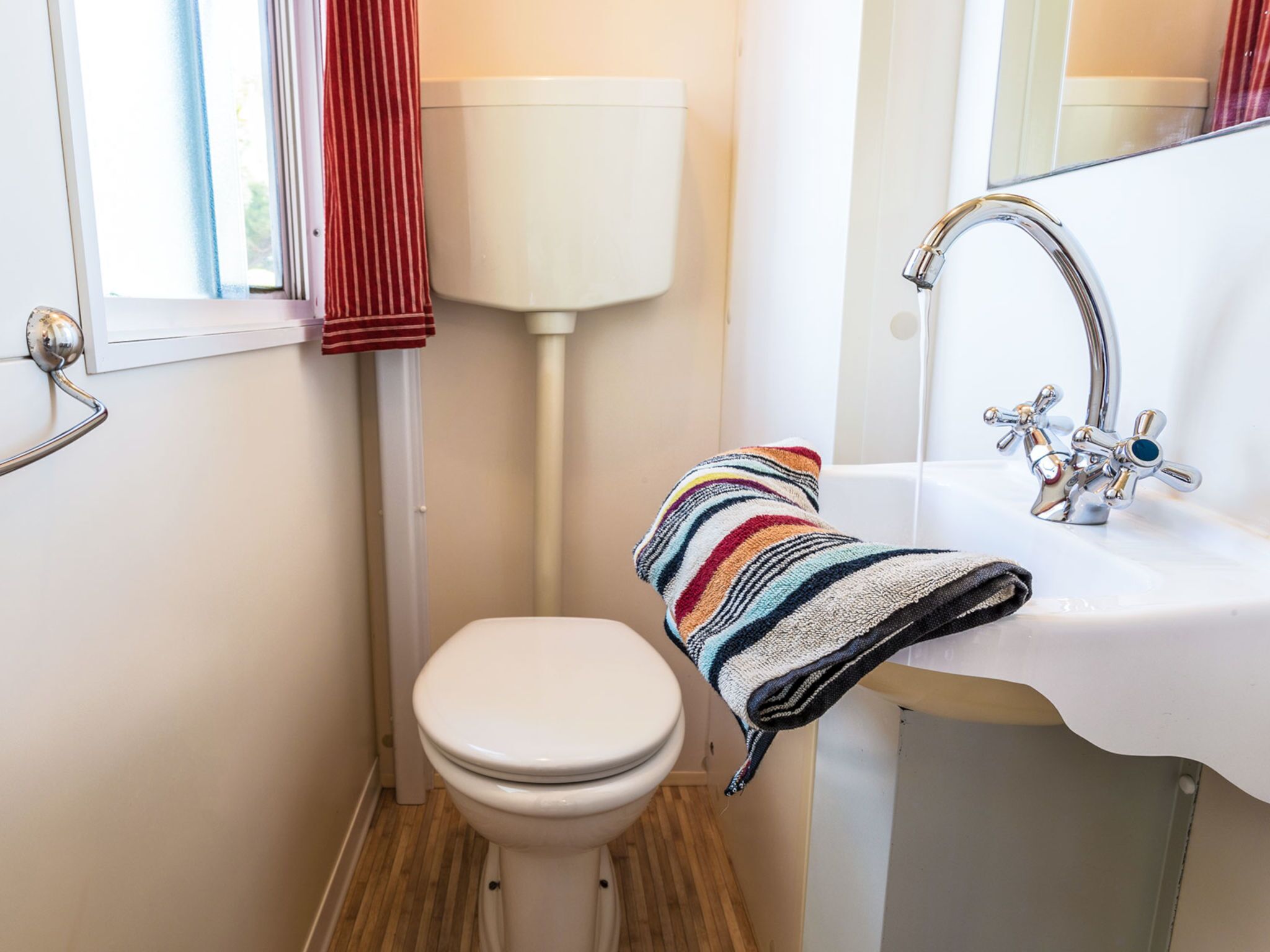 A small bathroom with a white toilet, a sink with a chrome faucet, and a striped towel hanging on the wall.
