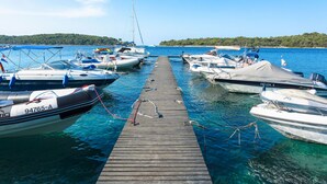 Une jetée où sont amarrés plusieurs bateaux, un ciel bleu dégagé et, au loin, une côte bordée d’une forêt.