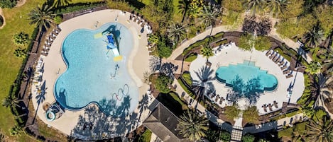 An aerial view of a resort with two swimming pools, palm trees, and lounge areas.