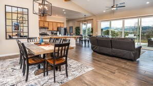 A spacious living area with a large sofa, dining table, and chairs. There is a kitchen area with wooden cabinets and a ceiling fan. - Mountain View House with hot tub, putting green, stunning views! (Oakhurst)