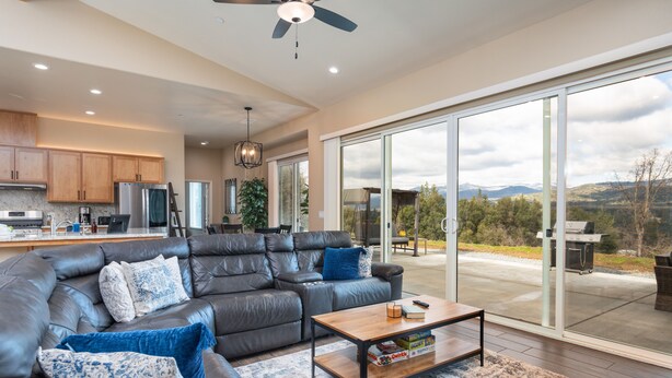 A modern living room with a leather sectional sofa, a coffee table, and a view of the outdoors through large sliding glass doors. - Mountain View House with hot tub, putting green, stunning views! (Oakhurst)