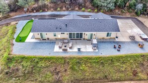 An aerial view of a two-story building with a patio area, outdoor seating, and a hot tub. - Mountain View House with hot tub, putting green, stunning views! (Oakhurst)