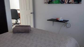 Un dormitorio con cama, puerta, silla, estante en la pared y un cuadro con una escena de canal.