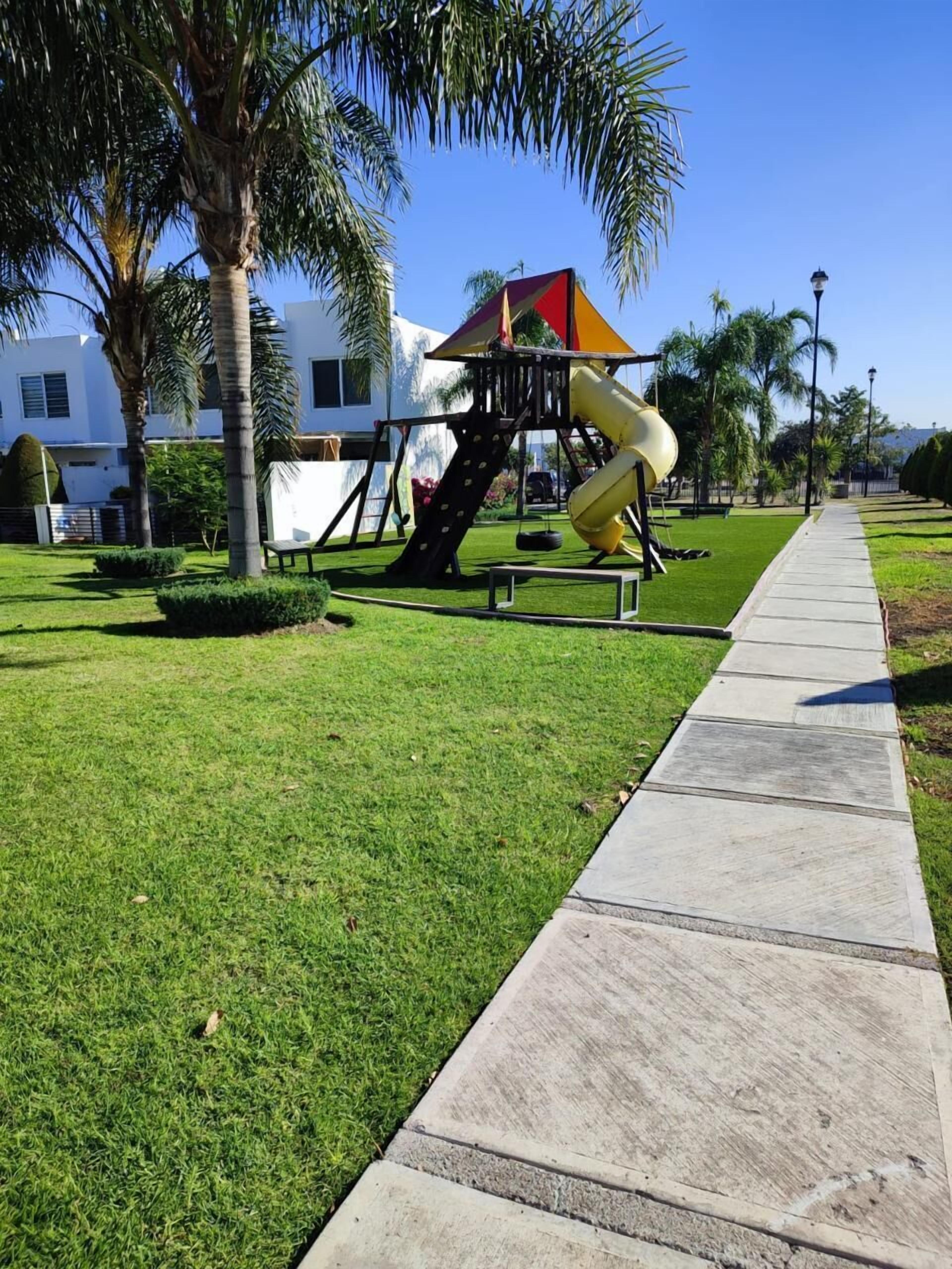 A playground with a slide and climbing structure, surrounded by well-maintained grass and palm trees.