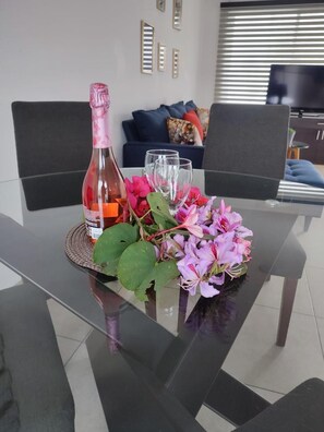Une table à manger avec une bouteille, des verres et un arrangement floral.