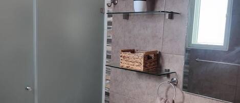 Un baño moderno con cabina de ducha de vidrio, inodoro, lavabo y espejo.