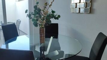 A modern dining area with a glass table surrounded by dark chairs, a vase with flowers, and a decorative wall piece.