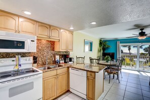 A kitchen with wooden cabinets, a microwave, stove, and dishwasher. There is a dining area with chairs and a table.
