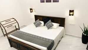 A neatly made bed with a wooden headboard, two wall-mounted lights, and a potted plant beside the bed. - Ibeeza Motel (Batigama)