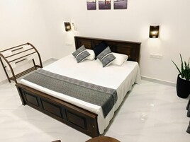 Una cama bien tendida con cabecera de madera, dos luces fijadas a la pared y una planta en maceta al lado de la cama.
