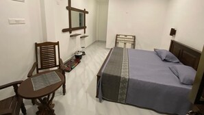 A bedroom with a bed, a chair, a small table, a mirror, and a bedside table. - Ibeeza Motel (Batigama)