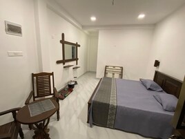 Un dormitorio con una cama, una silla, una mesita, un espejo y una mesita de noche.