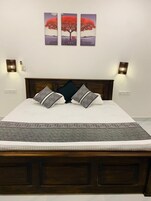 Un dormitorio con cabecera de madera, una cama con ropa de cama estampada y tres cuadros colgados en la pared de un árbol.