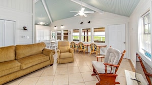 A spacious living room with a high ceiling, a large window, and a dining area with chairs and a table. - Milky Way Beach Front: Coastal Realty Group (Grand Isle)