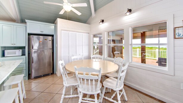 A kitchen with white cabinets, a stainless steel refrigerator, a microwave, and a dining table with white chairs. - Milky Way Beach Front: Coastal Realty Group (Grand Isle)