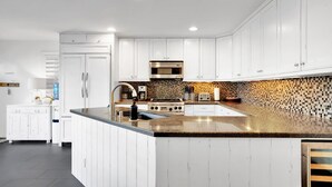 A modern kitchen with white cabinetry, a central island, stainless steel appliances, and a mosaic backsplash. - Fantastic Bayside Vacation Home w/ WiFi, Private Washer/Dryer, Central AC, Patio (San Diego)