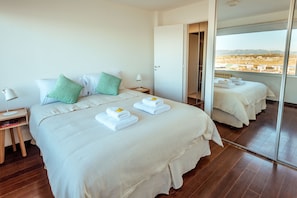 A hotel room with a large bed, a nightstand, a lamp, and a view of the city through a large window.
