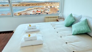 A hotel room with a large window offering a view of a river and distant buildings. The bed is neatly made with white linens and pillows. - Moat Apartamento (Ushuaia)