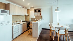 A modern kitchen with wooden cabinets, a built-in oven, and a dining area with a white table and chairs. - Moat Apartamento (Ushuaia)