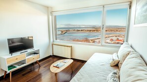 A modern room with a large window, a flat-screen TV, a wooden coffee table, and a sofa with patterned cushions. - Moat Apartamento (Ushuaia)