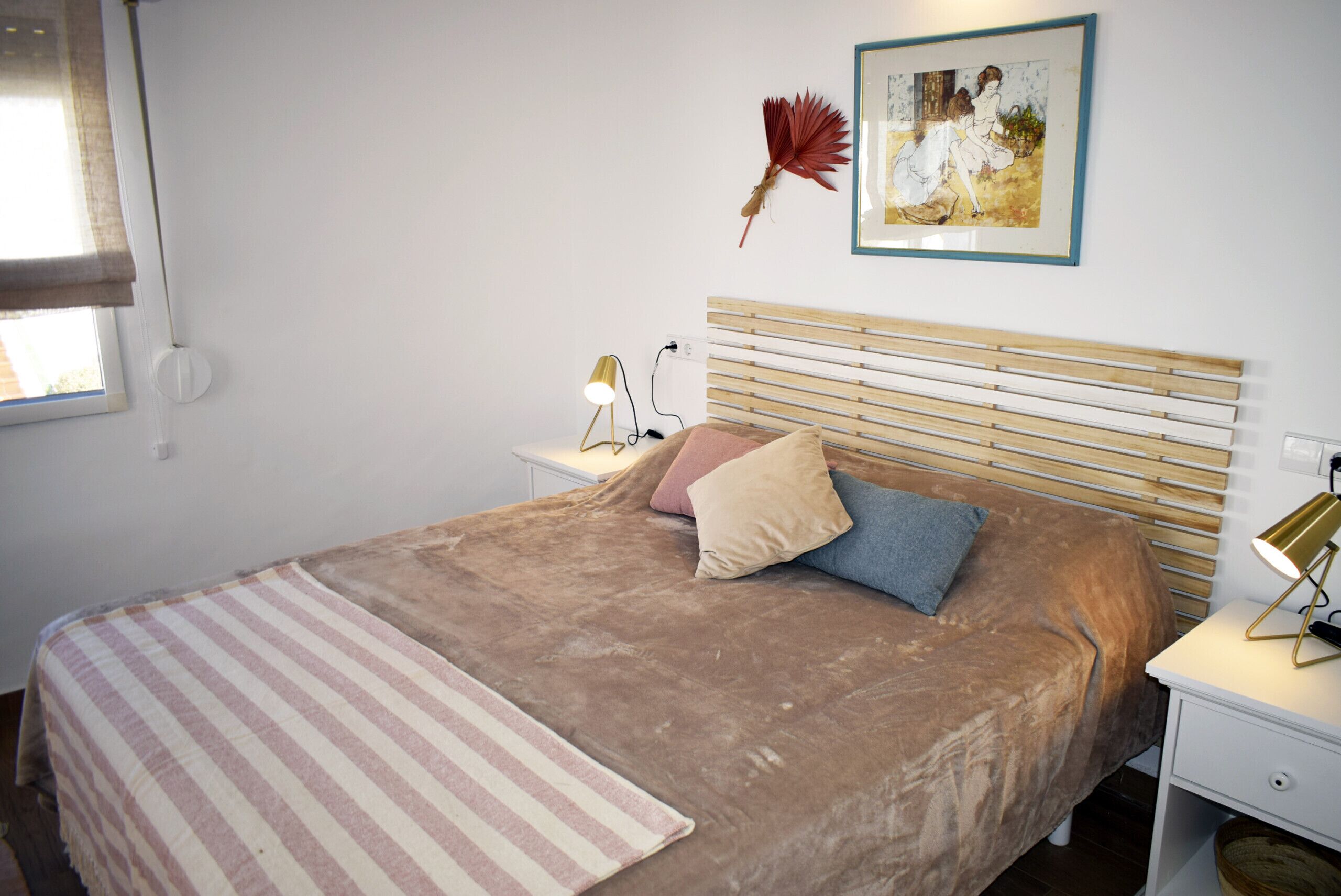 Una camera da letto con un letto, un comodino, una lampada, un quadro incorniciato e una finestra con tende.