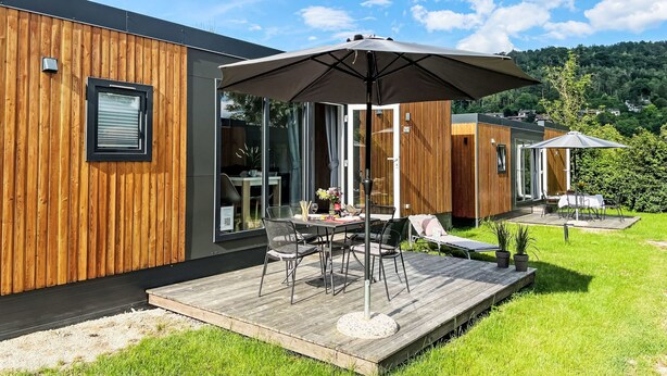 A modern outdoor patio with a wooden deck, a table with chairs, and a large umbrella. - Tiny Haus Sonnenplatz by Interhome (Riedenburg)