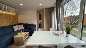 A modern living room with a dark blue sofa, a wooden coffee table, and a glass dining table with two chairs. There is a large window providing a view of the outside. - Tiny Haus Sonnenplatz by Interhome (Riedenburg)
