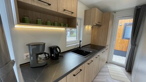 A modern kitchen with wooden cabinets, a black countertop, a coffee maker, and a window. - Tiny Haus Sonnenplatz by Interhome (Riedenburg)