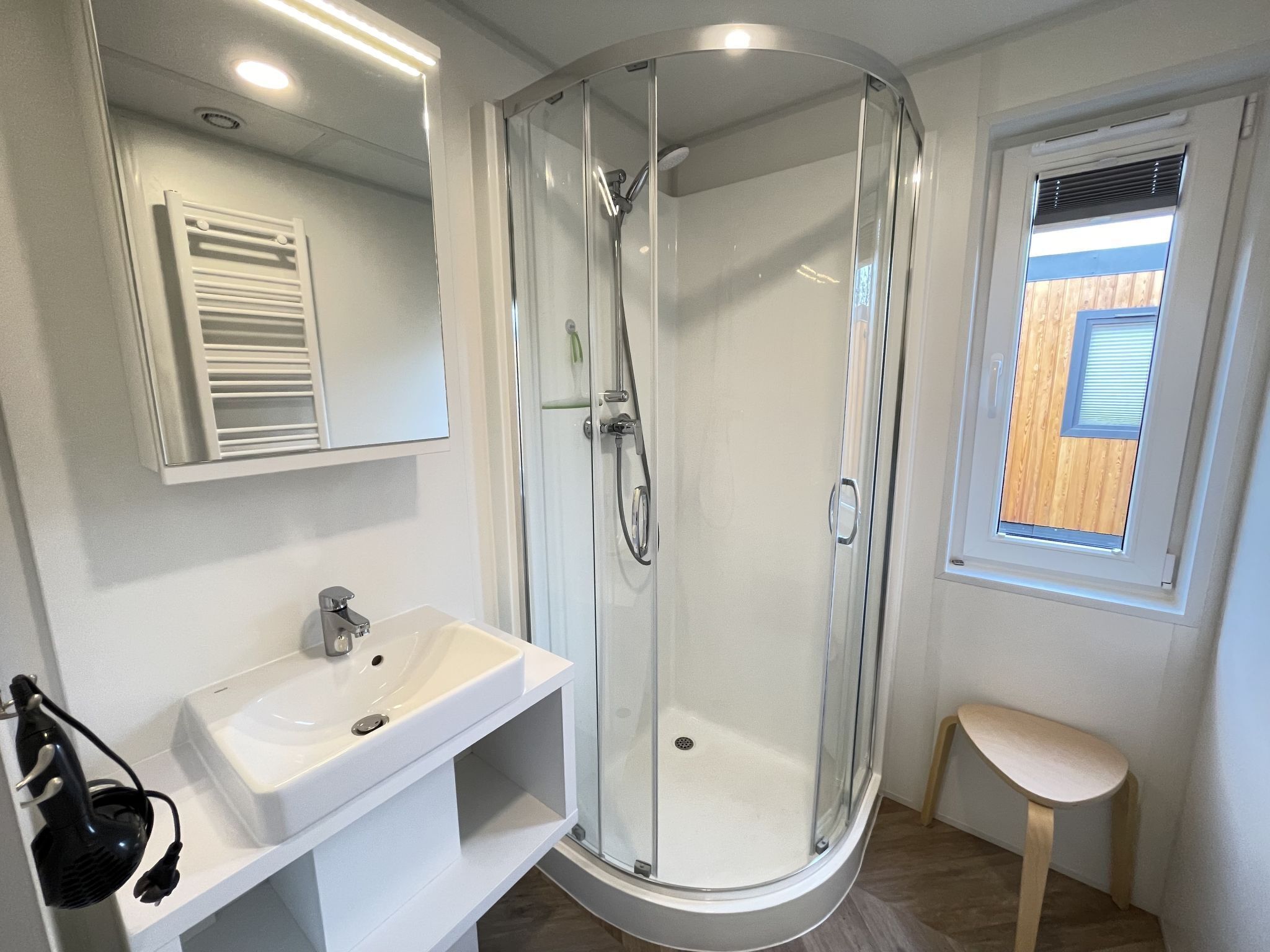 A modern bathroom with a glass-enclosed shower, a white sink, and a small stool.