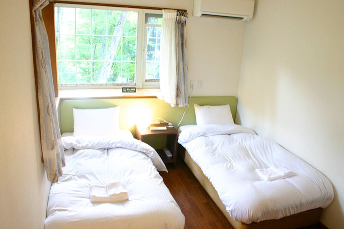 A room with two single beds, a nightstand with a lamp, and a window with curtains.