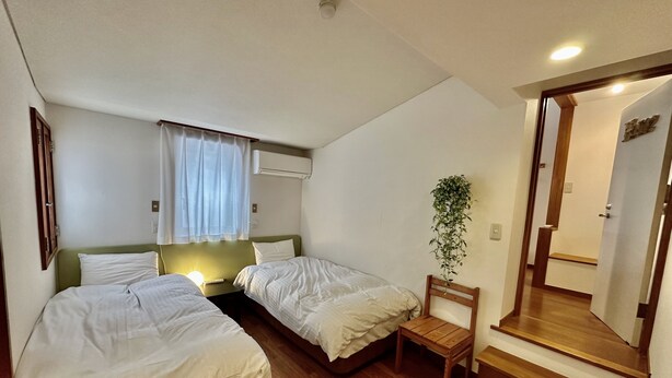 A hotel room with two single beds, a small table, a chair, a potted plant, a mirror, and a wooden floor. - Windy Hill  (Yamanakako)