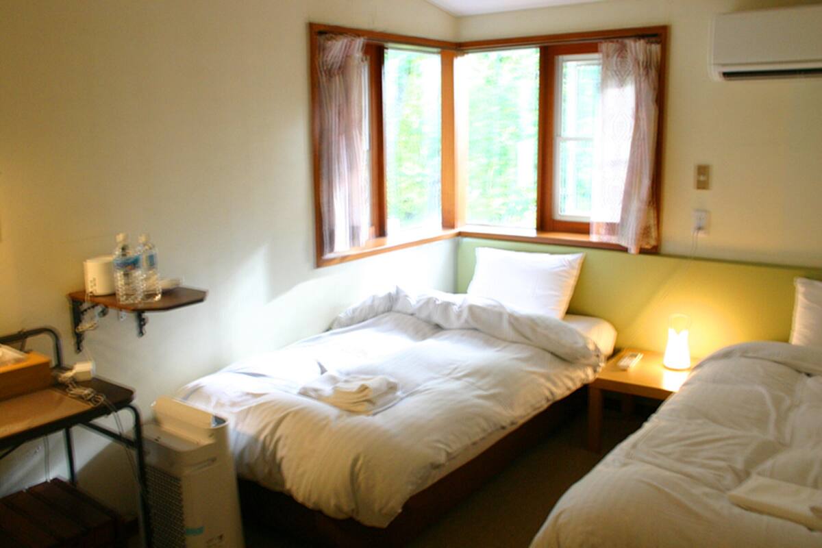A hotel room with two beds, a desk with a computer, a shelf with toiletries, and a window with curtains.