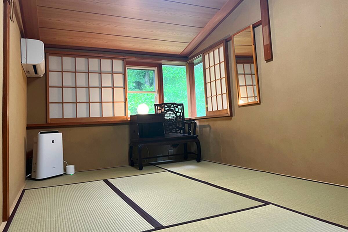 A traditional Japanese room with tatami flooring, a low table with a black chair, and sliding doors with glass panels.