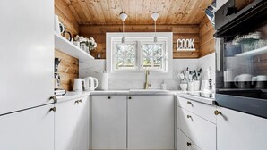 A kitchen with white cabinets, a black refrigerator, a window with a view of trees, and a 'COOK' sign on the wall.