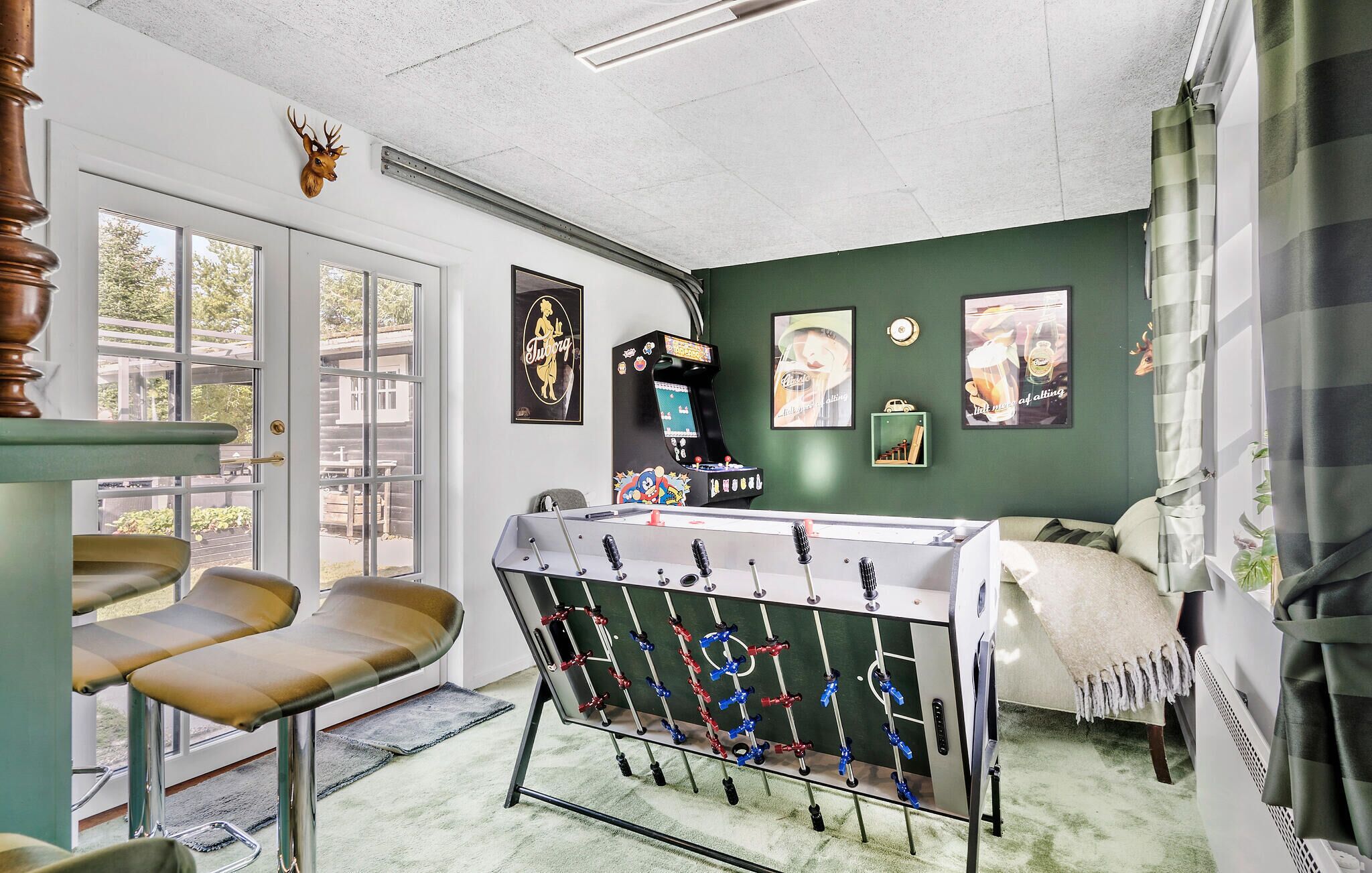 A room with a foosball table, a bar area, and a green wall with framed pictures.