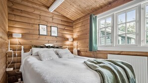 A cozy log cabin bedroom with a bed, two bedside lamps, framed pictures, and a window with curtains.