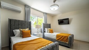 A hotel room with two beds, a TV, an air conditioner, and a window with curtains. - Modern 2BR near beach, dinning, and historic center, in the heart of the city (Puerto Plata)