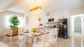 A modern kitchen with white cabinets, stainless steel appliances, and a glass dining table with white chairs. - Modern 2BR near beach, dinning, and historic center, in the heart of the city (Puerto Plata)