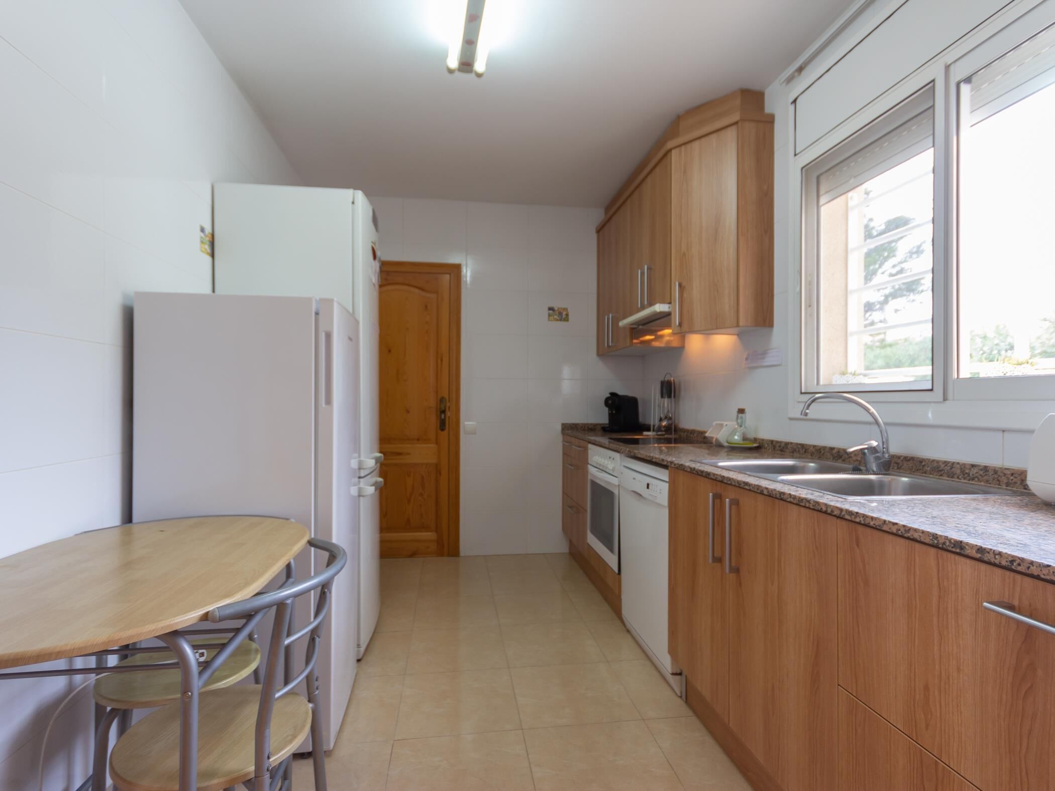 Una cocina compacta con armarios de madera, un refrigerador blanco, un fregadero y una zona de comedor con una mesa y sillas.