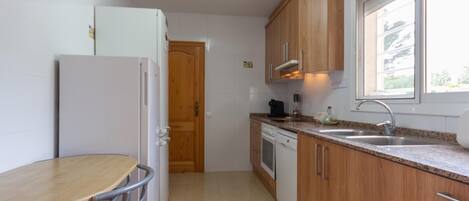 Una cocina compacta con armarios de madera, un refrigerador blanco, un fregadero y una zona de comedor con una mesa y sillas.