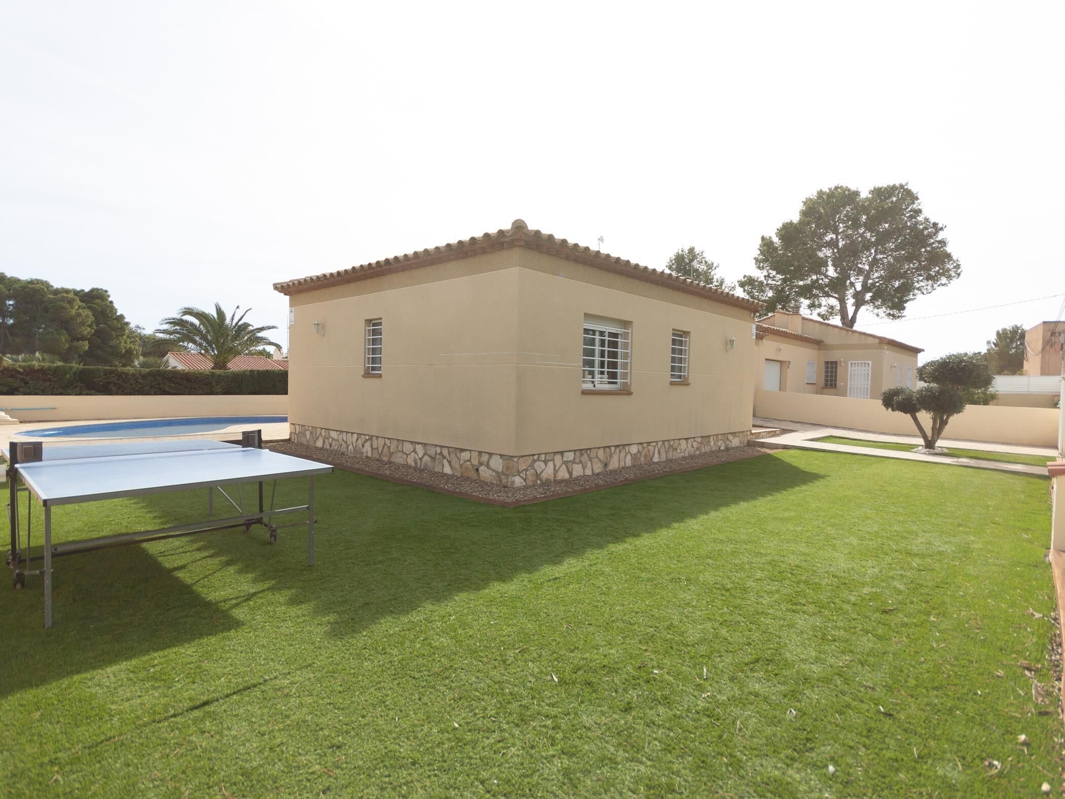 Une maison de plain-pied, avec des fondations en pierre et un toit en tuiles, entourée d’une pelouse bien entretenue et d’une piscine.
