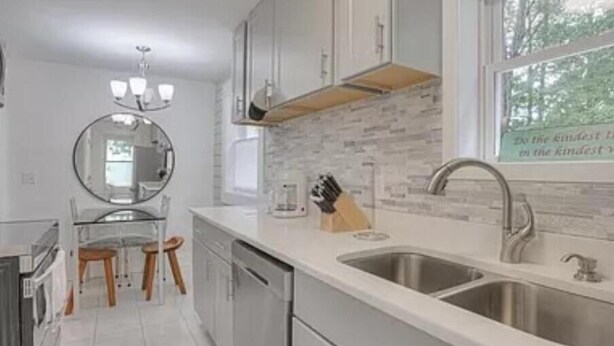 A modern kitchen with white cabinets, a double sink, and a window with a view of trees.